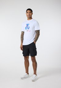 White t-shirt with a colorful graphic design and text on the front, paired with black cargo shorts and white sneakers.
