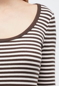 Csíkos, barna és fehér hosszú ujjú felső. Széles, kerek nyakkivágással és bordázott textúrával rendelkezik. A vízszintes csíkok végig egységesek.