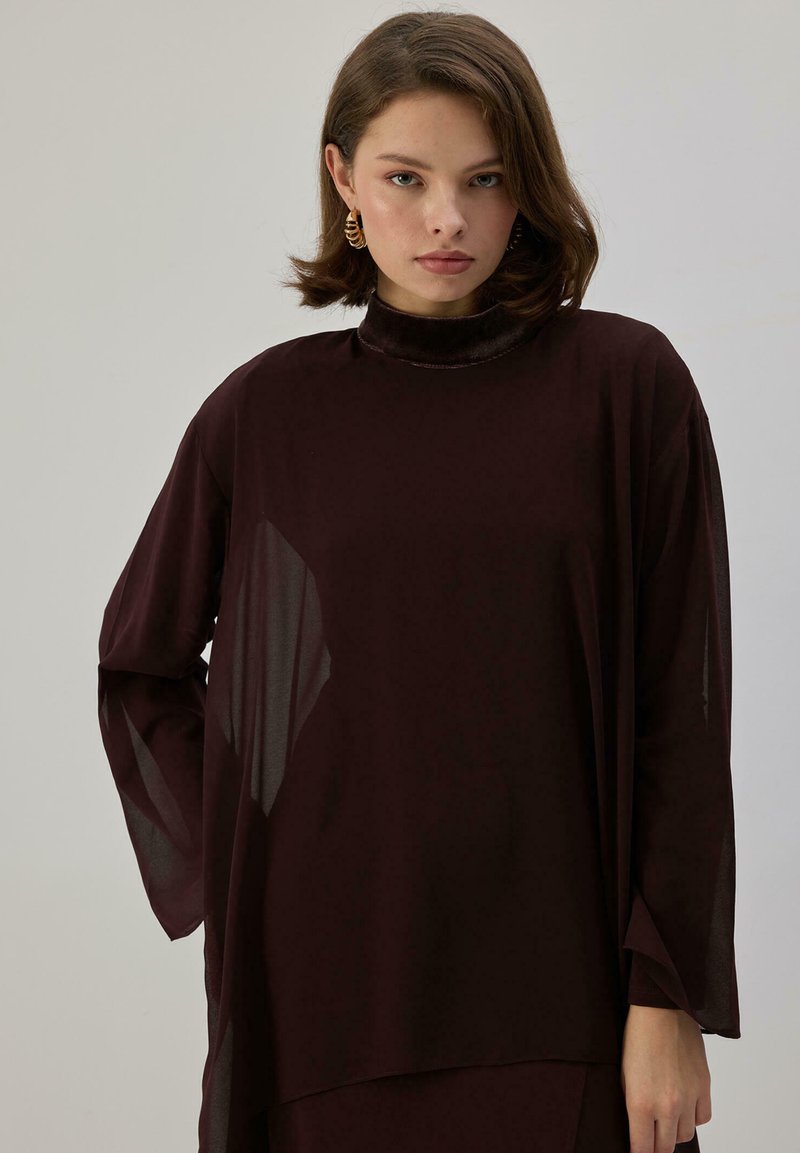 Maroon blouse with long sleeves and a high collar, featuring sheer panels, smooth texture, and a loose fit for comfort.