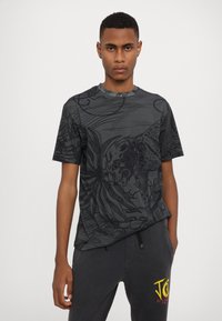 T-shirt graphique noir avec des motifs animaliers et floraux complexes. Tissu en coton, manches courtes, col rond, coupe décontractée.