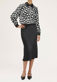Gonna a matita nera in seta abbinata a una blusa a righe bianco e nera con colletto in paillettes nere. Tacchi a spillo neri completano l'outfit.