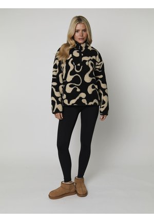 Suéter de forro polar negro y crema con un patrón abstracto, cuello alto y cierre de media cremallera. Combinado con leggings negros y botas color tostado.