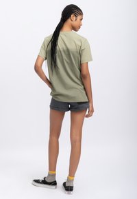 Olive green cotton t-shirt with short sleeves, slightly loose fit, paired with dark gray shorts and black sneakers, showcasing a relaxed style.