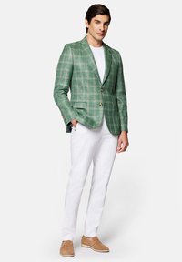 Zielona marynarka w kratę z wykładanym kołnierzem, dwoma przednimi kieszeniami i złotymi guzikami, zestawiona z białą koszulką i białymi spodniami. Brązowe buty.