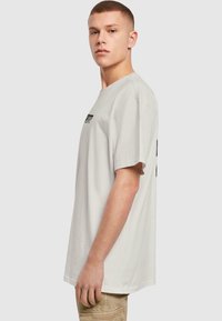 Lys grå oversized t-shirt med korte ærmer, rund halsudskæring, og sort grafisk tekst på fronten. Blødt bomuldsstof, afslappet pasform.