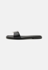 Svarta platta sandaler i läder med en bred rem och en metallisk detalj vid tån, med en minimalistisk design och gummisulor.