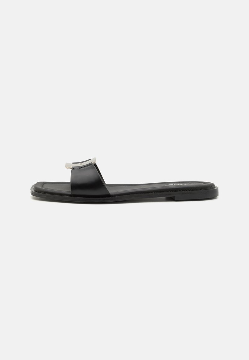 Svarta platta sandaler i läder med en bred rem och en metallisk detalj vid tån, med en minimalistisk design och gummisulor.