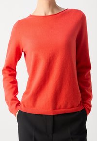 Pull en tricot rouge à manches longues, col arrondi et poignets côtelés, associé à un pantalon noir. Texture douce, design minimaliste, sans motif.