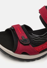 Raudoni ir juodi šlepetės su reguliuojamais dirželiais, minkšta medžiaga, tekstūruotas padas ir guminis padas su bangų raštu.