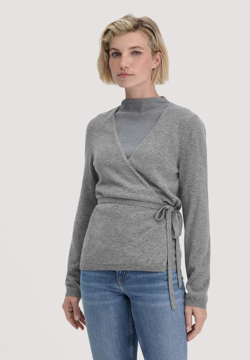 Grauer Wickelpullover aus weichem Material, mit langen Ärmeln, einem Bindegürtel in der Taille und einem V-Ausschnitt. Getragen über einem grauen Oberteil.