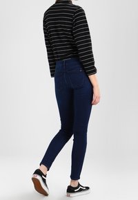 Tummansininen denimi skinny-farkut korkealla vyötäröllä, yhdistettynä musta-valkopaitaan pitkällä hihalla ja mustiin lenkkikenkiin.