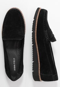 Svarta mocka loafers med moccasindesign, med dekorativ söm, kontrasterande brun gummisula och perforerad innersula.