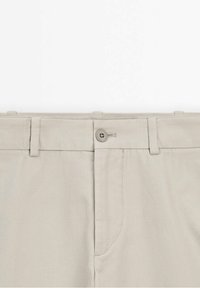 Beiga byxor med knappstängning, slät front, bältesöglor och sidofickor. Tyget verkar slätt och lätt.