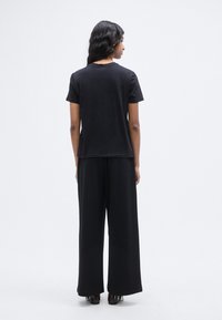 Μαύρο κοντομάνικο μπλουζάκι με χαλαρή εφαρμογή, συνδυασμένο με μαύρο παντελόνι φαρδιάς γραμμής. Λείο ύφασμα, μινιμαλιστικός σχεδιασμός χωρίς ορατά σχέδια.