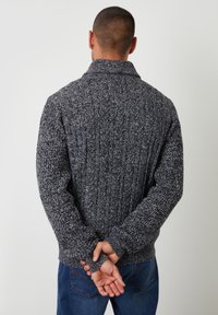 Maglione tricotato in grigio scuro e bianco, con una texture a costine e un colletto a scialle. Maniche a vestibilità rilassata e orlo inferiore solido.