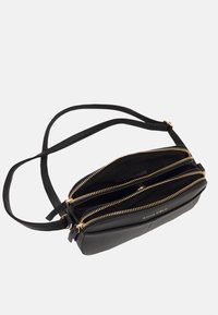 Černá kožená crossbody taška se třemi zipovými přihrádkami, zlatými zipy a hladkým povrchem. Součástí je nastavitelné rameno.