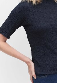 Marinblus med korta ärmar, i strukturerad design, med ett rynkat mönster och en figurnära siluett, matchad med mörka jeans.