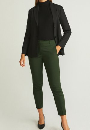 Svart kavaj, tajt svart polotröja, gröna byxor och svarta spetsiga klackar. Byxor med smal skärning, mjuk textur och minimalistiska detaljer.