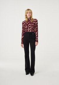 Langarmtop in bordeaux met abstract crèmekleurig patroon, gecombineerd met hoge zwarte flared broeken met een subtiele gouden accenten.