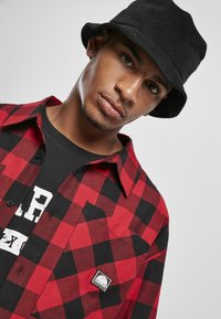 Rød og sort ternet flannel skjorte med en sort crew neck under, prydet med et lille logo patch og en sort kordfløjl bucket hat.