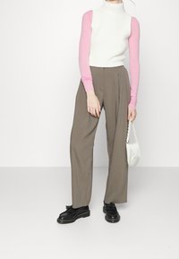 Maglione con collo alto di colore crema, maniche lunghe rosa, pantaloni a gamba larga marroni, scarpe nere con frange, piccola borsa bianca con tracolla a catena.