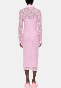 Abito in pizzo rosa con maniche lunghe, silhouette aderente, lunghezza a metà polpaccio, con tessuto trasparente e dettaglio con lacci sul retro.