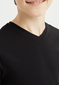 T-shirt in cotone nero con scollo a V, caratterizzato da una trama liscia e una forma aderente, che mette in risalto la scollatura e la zona delle spalle.