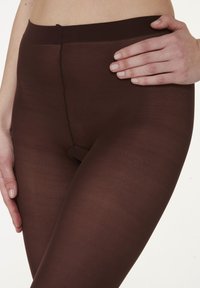 Braune Leggings aus einem glatten, dehnbaren Material, mit hohem Bund und minimalen Nähdetails, eng an den Beinen anliegend.