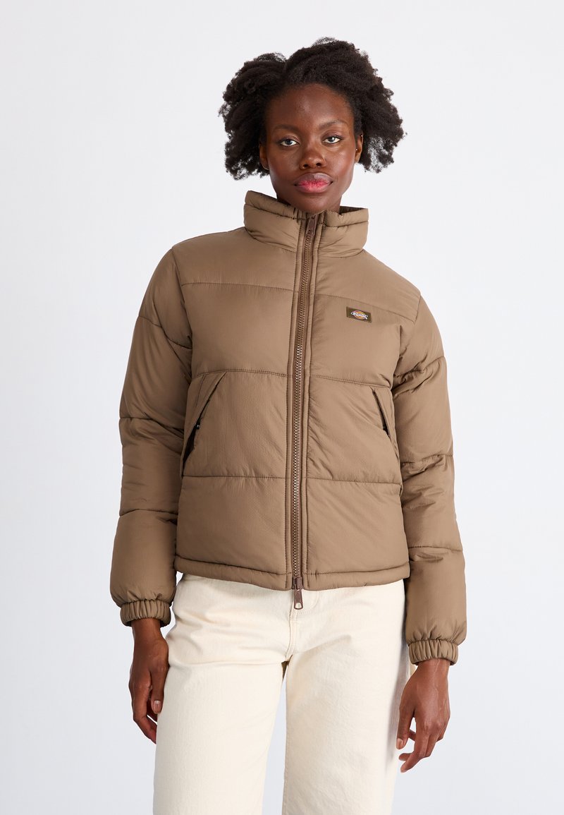 Giubbotto imbottito marrone con colletto alto, chiusura a zip, polsini elasticizzati e tasche laterali. Presenta un design trapuntato e un logo ricamato sul petto.