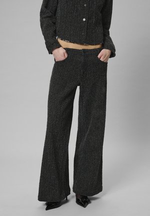 Schwarze Tweedjacke mit einem verkürzten Design und Knopfverschluss, kombiniert mit schwarzen weit geschnittenen Hosen mit Seitentaschen und strukturiertem Finish.