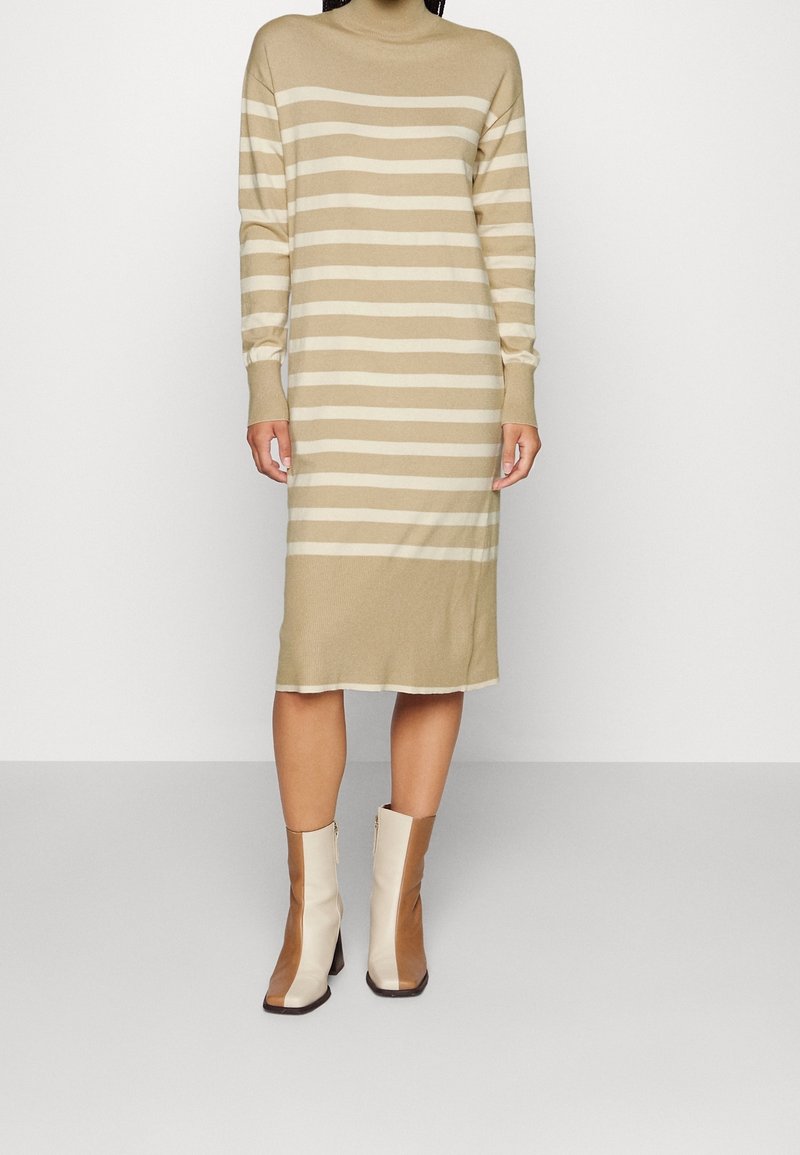 Personne portant une robe midi à manches longues rayée beige et blanche avec des bottines à enfiler beige et blanches à empiècements colorés.