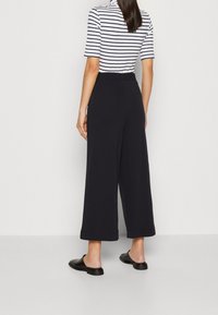 Vida svarta byxor med vida ben och en slät textur, utrustade med resårlinning. Matchas med en randig topp och svarta slip-on skor.