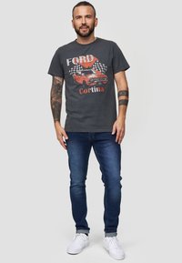 Grå T-shirt med trykt Ford Cortina grafik, suppleret med blå jeans og hvide sneakers. Enkel crew-neck design.