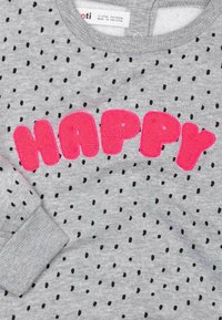 Harmaa huppari, jossa on mustia pilkkuja ja vaaleanpunaiset pehmeät "HAPPY"-tekstit. Ribbattu kaula-aukko ja hihansuut, pehmeä kangas, sopii lapsille.