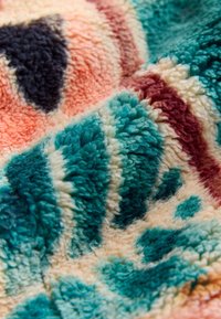 Weicher, plüschiger Stoff mit Türkis, Creme, Burgunder, Schwarz und Korallenfarben in einer flauschigen, gemusterten Textur.