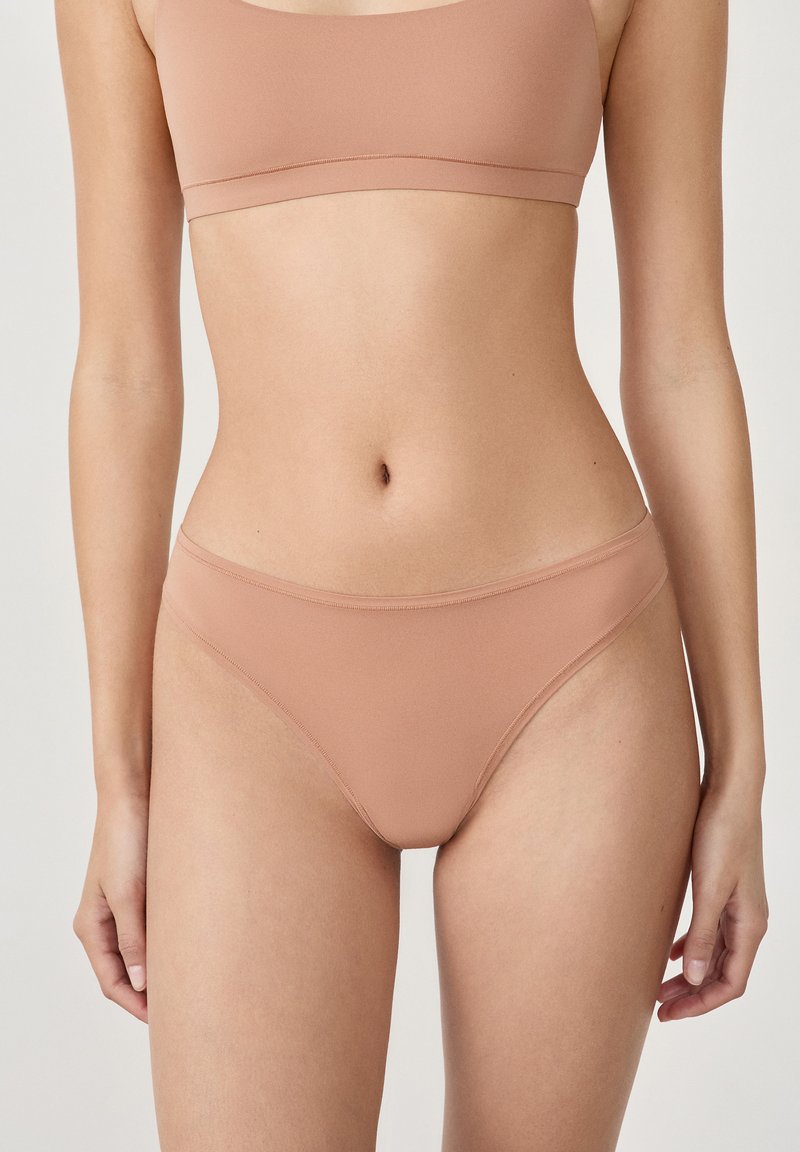 Beżowa, gładka bielizna bikini o niskim kroju, wykonana z miękkiego materiału, o minimalistycznym designie. Bez widocznych szwów i ozdób.