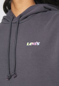 Gros plan sur un sweat à capuche gris avec un logo Levi’s coloré sur la poitrine et des cordons pendants.