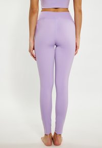 Lila leggings sima, rugalmas textúrával, testhezálló formával és boka hosszúságú kivitelezéssel. Nincsenek látható varratok vagy minták.