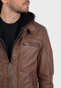 Giacca di pelle marrone con zip frontale, tasca sul petto e colletto a pressione. L'interno presenta una fodera in pile nera. Superficie texture.