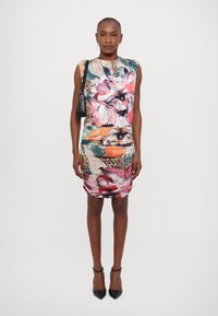 Abito con stampa floreale caratterizzato da colori vivaci, una silhouette aderente e dettagli arricciati. Abbinato a scarpe nere con tacco a punta.