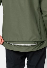 Giacca verde oliva con una tasca con zip all'orlo. Il tessuto appare liscio, con una fodera interna leggermente lucida.