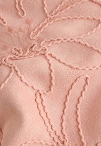 Tissu rose doux avec broderie en fil torsadé en relief formant un motif floral abstrait.