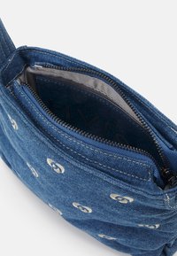 Sac bandoulière en denim bleu avec des cercles blancs brodés et une fermeture éclair noire partiellement ouverte montrant une doublure intérieure gris clair.