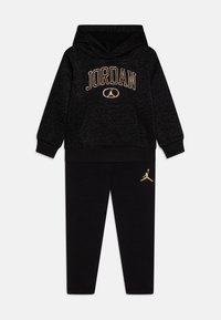 Černá mikina s kapucí s nápisem "JORDAN" a logem vyšitým zlatou nití a černé teplákové kalhoty s výrazným zlatým logem na levé noze. Vyrobeno z měkkého materiálu.