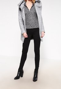 Szary płaszcz z wełny z kapturem, wzorzysty czarny sweter, czarne skinny jeans oraz czarne botki na obcasie. Prosty, nowoczesny design.