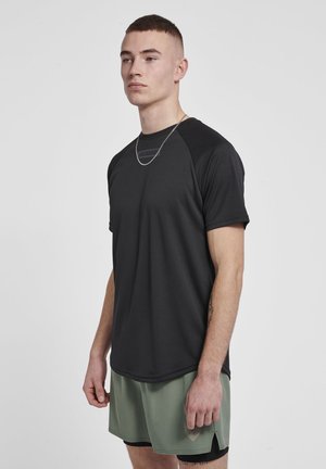 Musta urheilupaita lyhyillä hihoilla ja raglan-muotoilulla, valmistettu hengittävästä kankaasta. Yhdistetty vaaleanvihreisiin shortseihin. Yksinkertainen pyöreä pääntie.