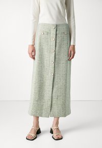 Grønn tweed midi-skjørt med teksturert stoff, frontknapplukking og sidelommer. Kombinert med beige sandaler med blokkhæl og stropper.