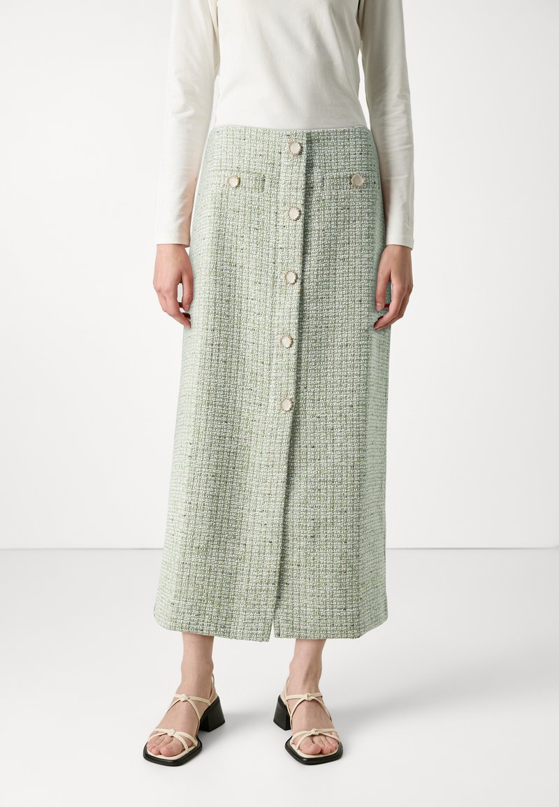 Grønn tweed midi-skjørt med teksturert stoff, frontknapplukking og sidelommer. Kombinert med beige sandaler med blokkhæl og stropper.
