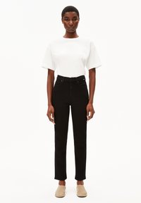 Jean noir taille haute avec une jambe droite, associé à un t-shirt blanc à manches courtes et des chaussures slip-on beige clair.