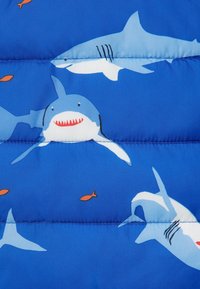 Tessuto blu a imbottitura con un motivo di squali ripetuto in diverse tonalità di blu, con accenti rossi e piccoli pesci arancioni. Dettagli di cucitura visibili.